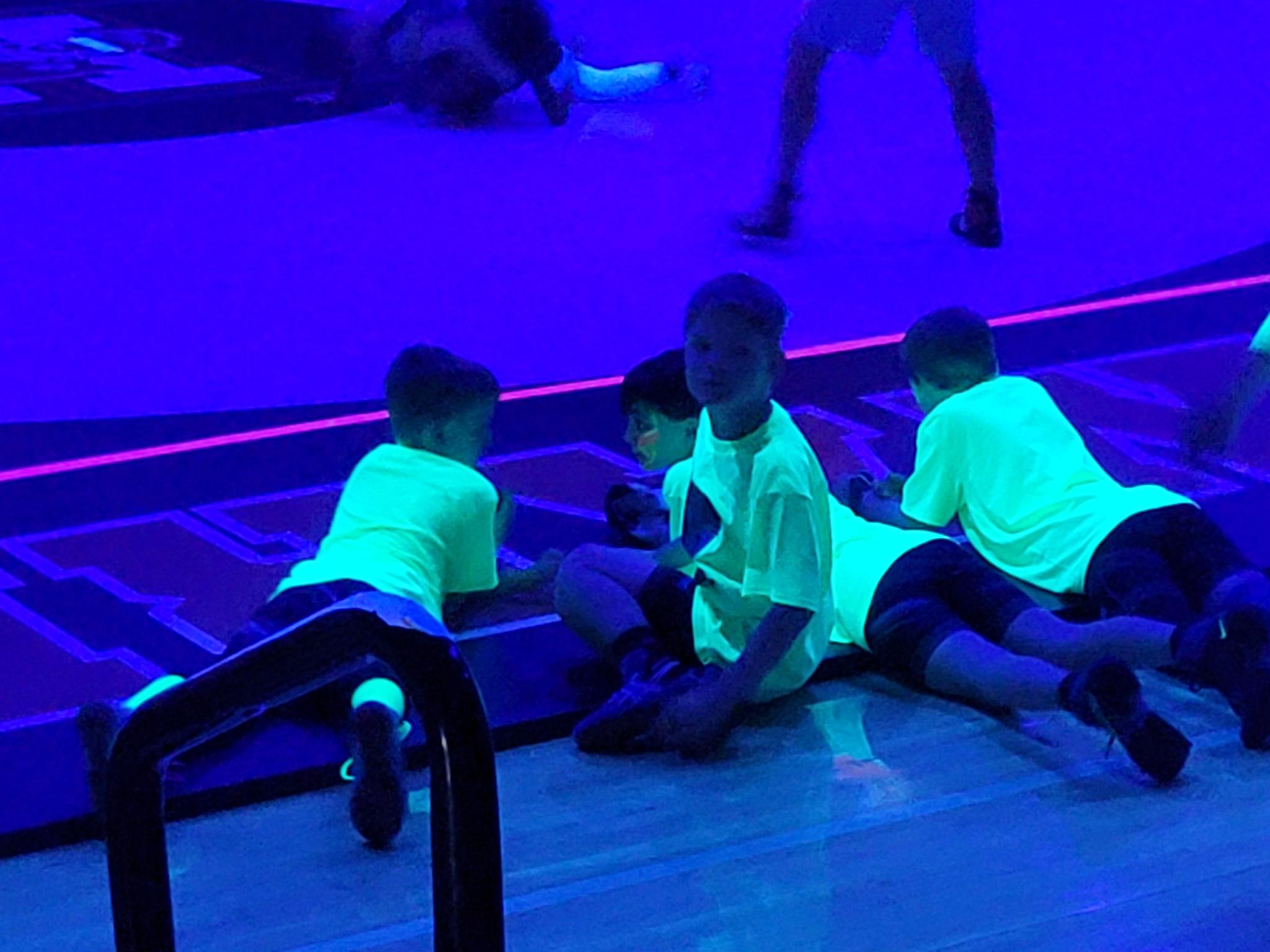 Young wrestlers matside under UV lights at Howard Tigers Blacklight Wrestling